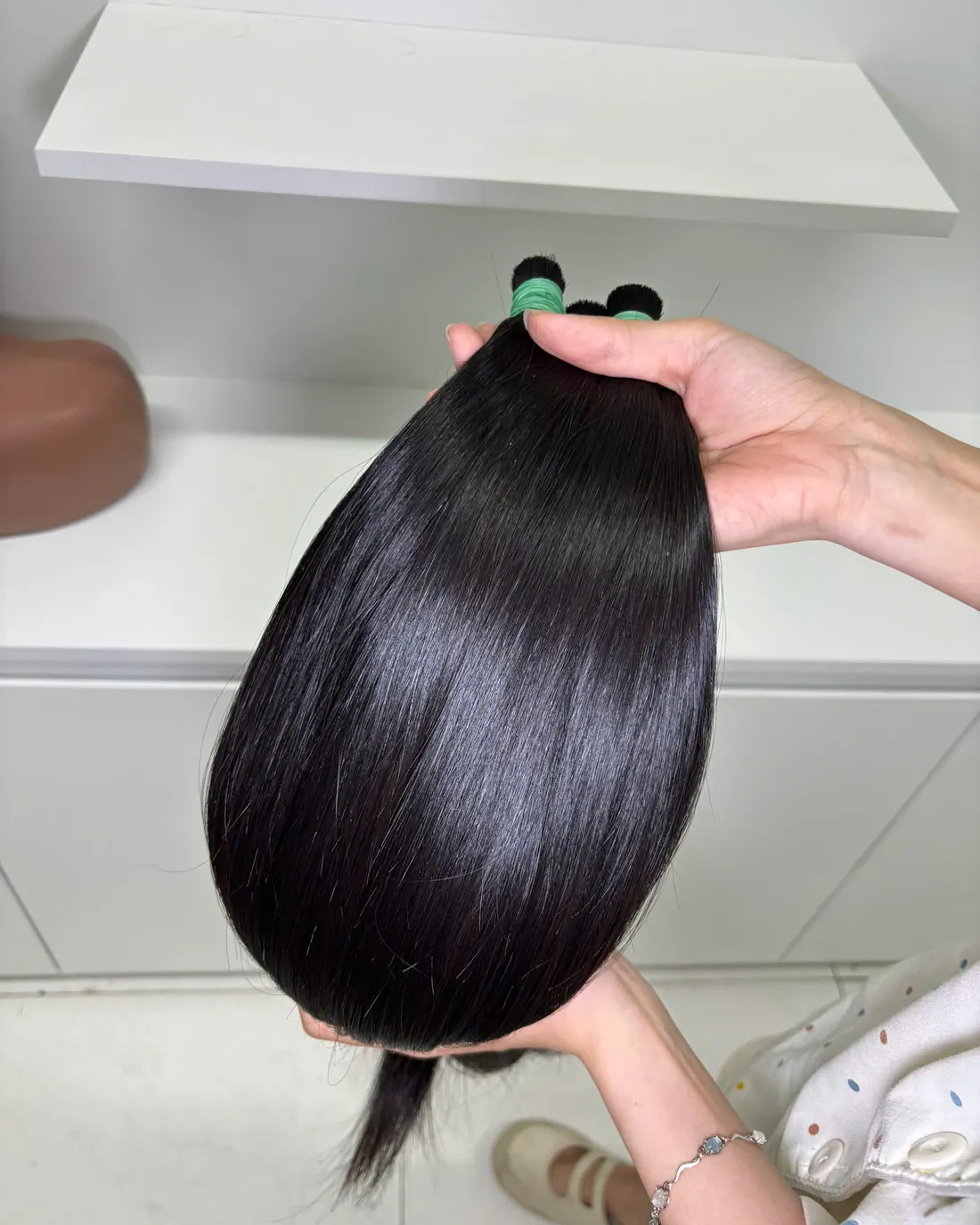 A handful of glossy, straight natural black human hair held up in our workshop
